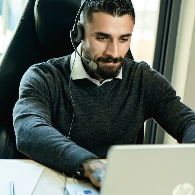 pexels-photo-7504858-7504858 Business professional with a beard using a laptop and headset at work. contact marketing digital